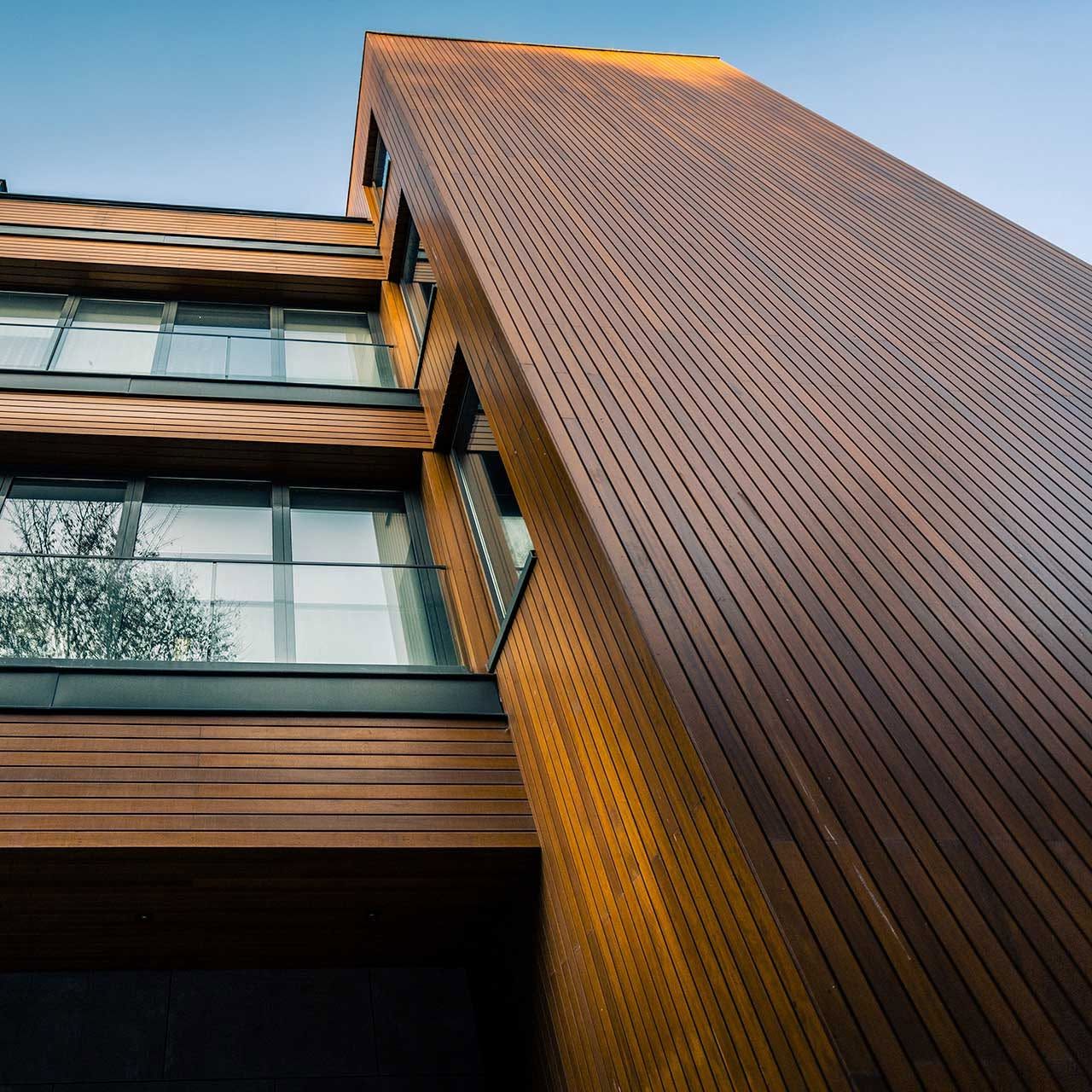 Modern building exterior with copper-toned metal siding and glass balconies against a blue sky.