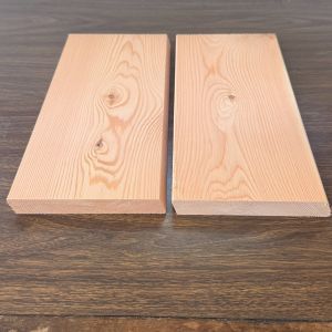 Two light wooden planks placed side by side on a dark wooden table, showing wood grain and knots.