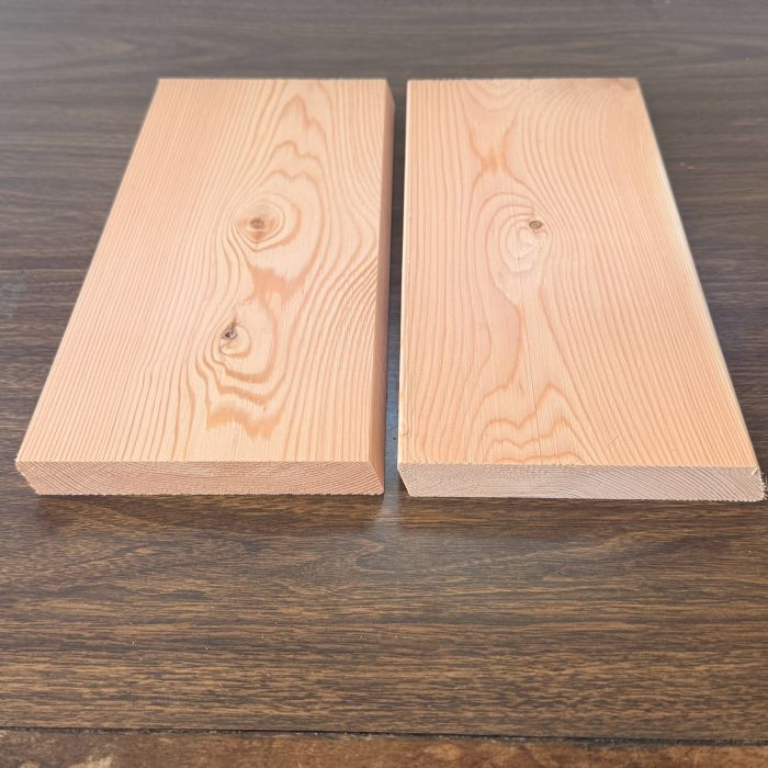 Two light wooden planks placed side by side on a dark wooden table, showing wood grain and knots.