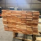 Stacks of orange-brown wooden boards stacked on a pallet in a warehouse workshop