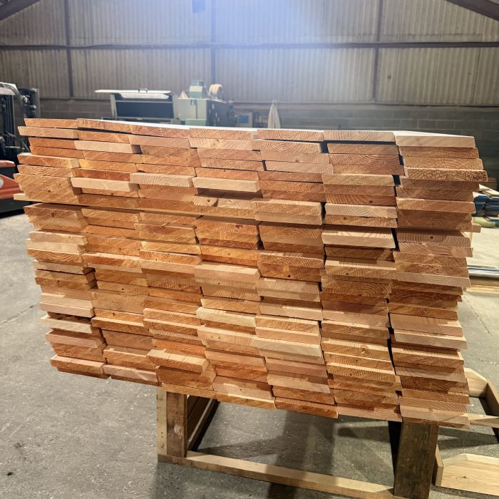 Stacks of orange-brown wooden boards stacked on a pallet in a warehouse workshop