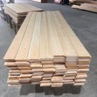Stacks of pale wooden boards neatly piled on pallets in a lumber warehouse, with a forklift visible in the background.