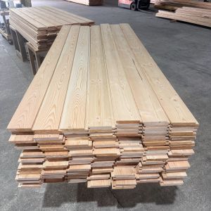 Stacks of light wood planks neatly piled on pallets in a warehouse, forklift visible in the background