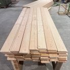 Stacks of long wooden planks on a workbench in a woodshop.