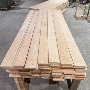 Douglas Fir Shadow Gap Cladding | Timberulove Stacks of long wooden planks on a workbench in a woodshop.